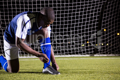 Male soccer player tying shoelace on field