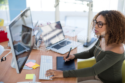 Female graphic designer working on computer while using graphic tablet at desk