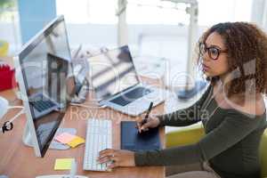 Female graphic designer working on computer while using graphic tablet at desk