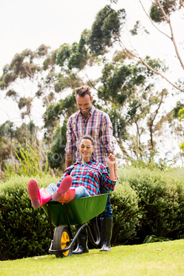 Man pushing young woman sitting in wheelbarrow