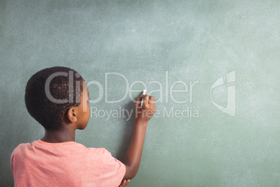 Boy writing with chalk on greenboard in school