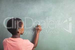 Boy writing with chalk on greenboard in school