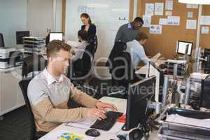 Businessman typing on keyboard while colleagues working in background