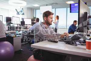 Young businessman working at desk while sitting on exercise ball