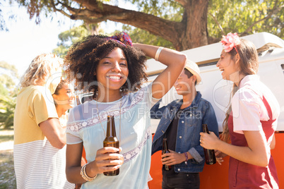 Portrait of woman holding beer bottle with friends in background