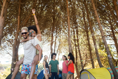 Happy man piggybacking woman with friends in background