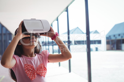 Schoolgirl using virtual reality glasses in corridor
