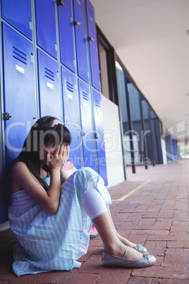 Side view of schoolgirl covering face with hands while sitting by lockers