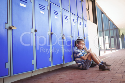 Side view of boy talking on mobile phone while sitting by lockers