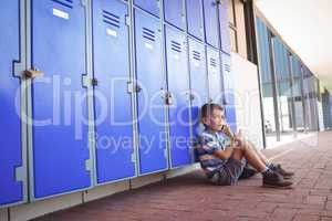 Side view of boy talking on mobile phone while sitting by lockers