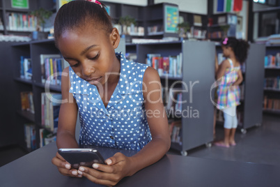 Girl using mobile phone at desk in library