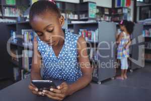 Girl using mobile phone at desk in library