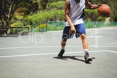 Low section of male teenager practicing basketball