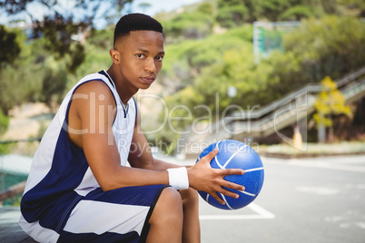 Portrait of teenage boy with ball sitting on bench