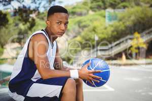 Portrait of teenage boy with ball sitting on bench