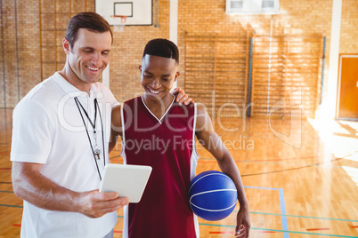 Smiling coach with player looking at tablet computer