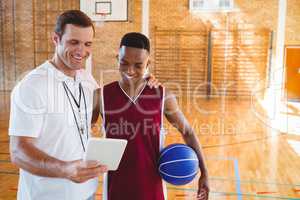 Smiling coach with player looking at tablet computer