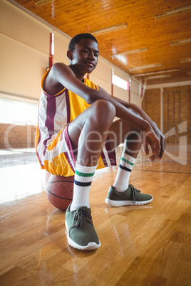 Confident teenage boy sitting on basketball