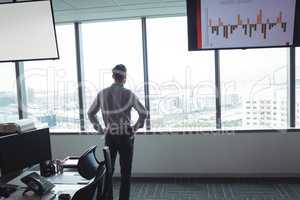 Rear view of businessman standing with hands on hip at office