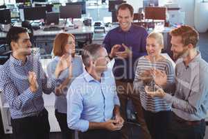 Happy businessman standing by colleagues clapping