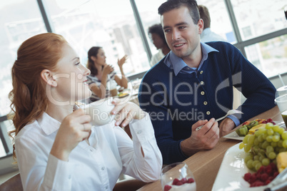 Young business colleagues talking at breakfast table in office
