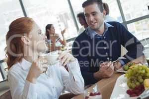 Young business colleagues talking at breakfast table in office