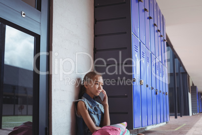Elementary schoolgirl talking on mobile phone while sitting by lockers