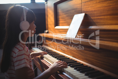 Girl looking at digital tablet while practicing piano in classroom