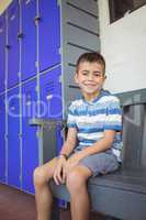 Portrait of smiling boy sitting on bench by lockers