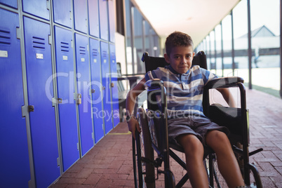 Portrait of boy sitting on wheelchair by lockers in corridor