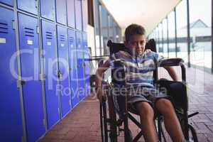 Portrait of boy sitting on wheelchair by lockers in corridor