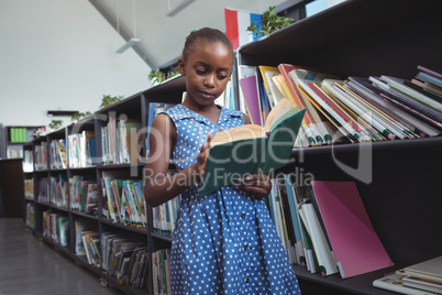 Girl reading book by bookshelf in library