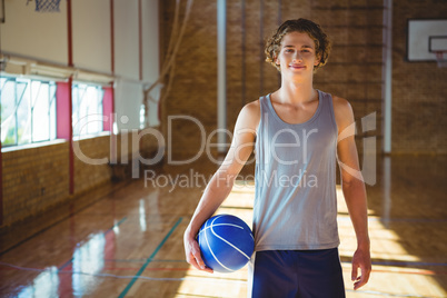 Portrait of smiling young man with basketball standing in court