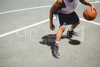 Low section teenage boy practicing basketball at court