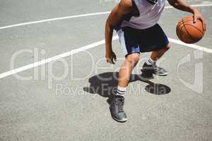 Low section teenage boy practicing basketball at court