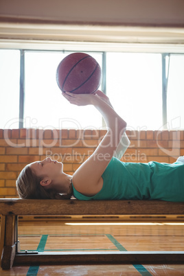 Female player playing with basketball while lying on bench in court