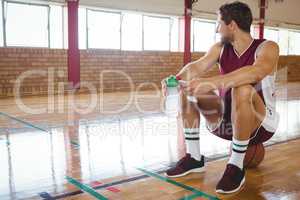 Male basketball player looking away while sitting on basketball