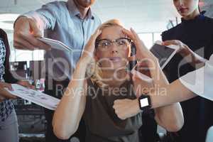 Frustrated businesswoman amidst team holding technologies