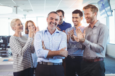 Happy businessman standing with arms crossed while colleagues clapping