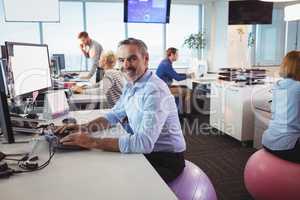 Portrait of smiling businessman working at desk while sitting on exercise ball