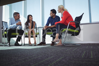 Business colleagues communicating while sitting on chairs at office