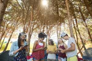 Happy friends using mobile phones at campsite