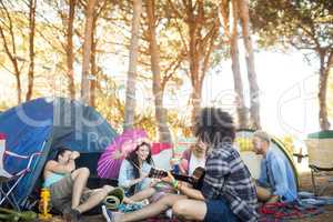 Man playing guitar while sitting with friends at campsite