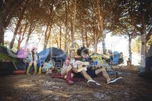 Young man with female friend playing guitar at campsite