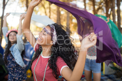 Woman with female friends holding scarfs at campsite