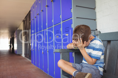 Unhappy boy sitting on bench in corridor