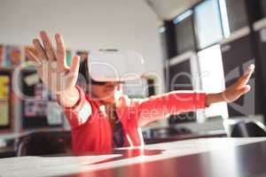 Girl gesturing while using virtual reality glasses in classroom