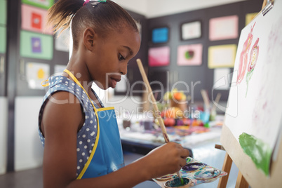 Side view of focused girl painting on canvas