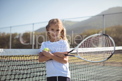 Confident girl holding tennis racket and ball at court