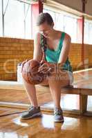 Smiling woman holding basketball while sitting on bench